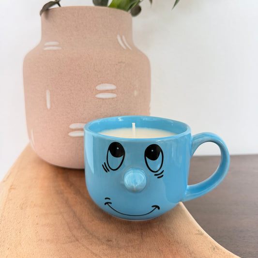 A light blue ceramic mug candle with a hand-drawn face